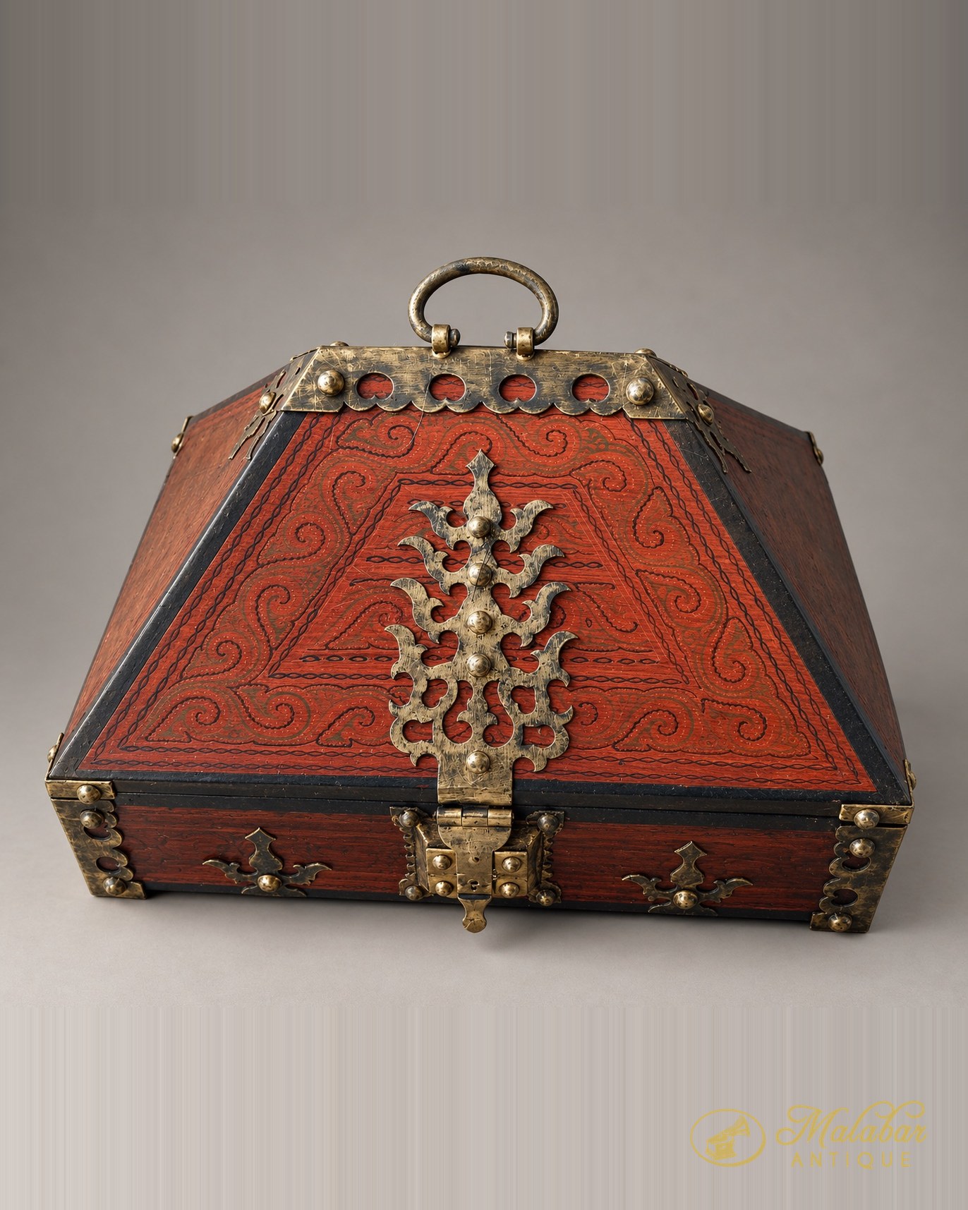 Red lacquered Kerala nettur petti with a sloping gabled lid, incised scrollwork, a foliate brass hasp and a ring handle.