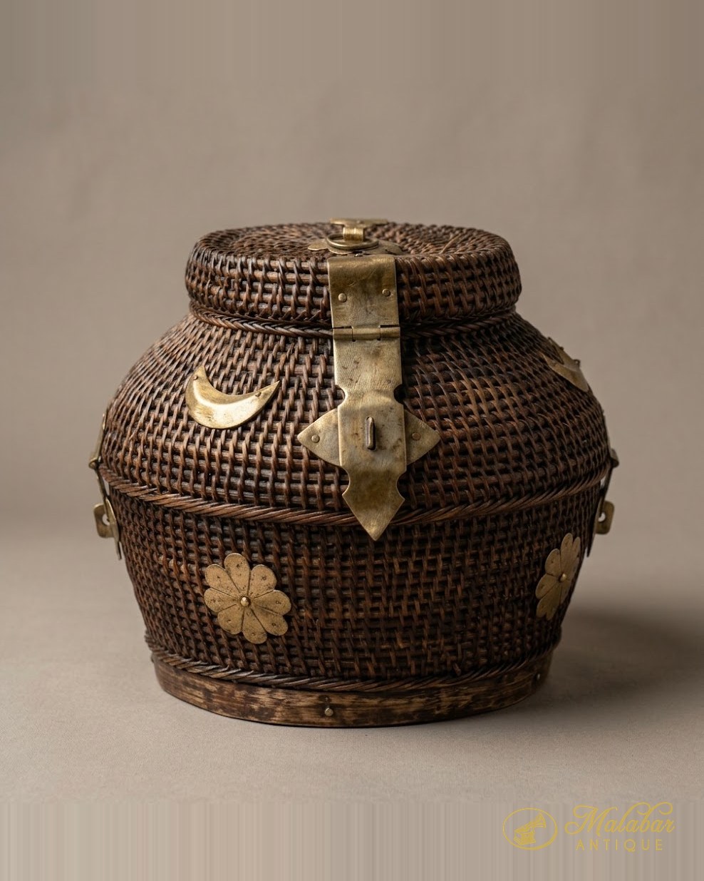 Lidded woven cane basket bound with a long brass hasp and applied brass crescent and flower mounts.