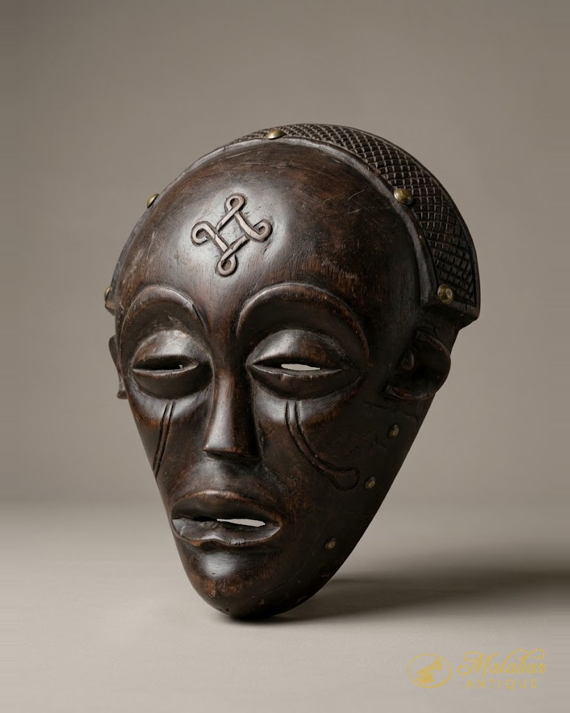 Dark hardwood face mask with heavy lidded eyes, incised cheek markings, a cruciform brow motif and a basket-woven crown studded with brass tacks.