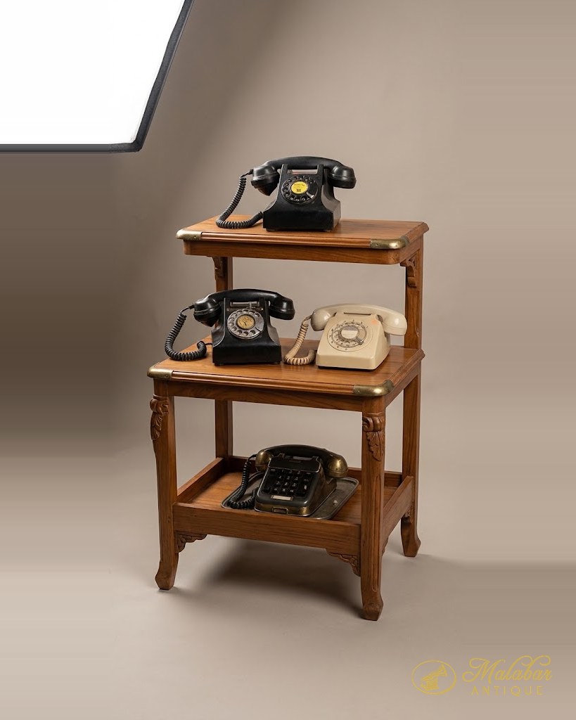 Three rotary dial telephones in black and ivory, on a two-tier wooden stand.