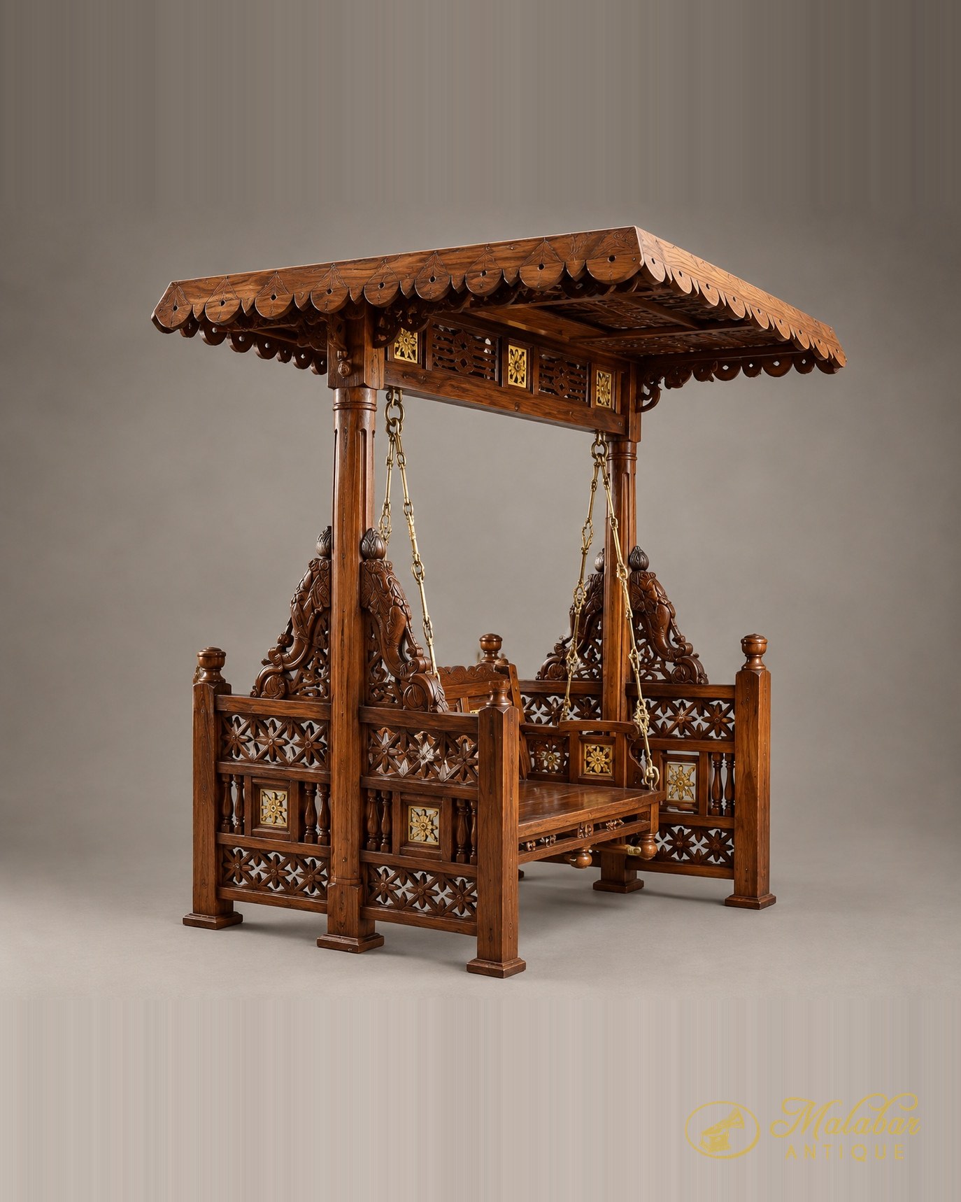 Carved teak swing seat with a tiled canopy roof, pierced floral panels, brass inlay medallions and brass suspension chains.