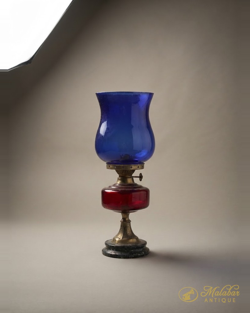 Table oil lamp with a cobalt blue shade over a ruby glass reservoir on a brass foot.