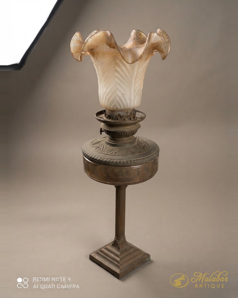 Brass oil lamp on a stepped column with a frilled opalescent glass shade.