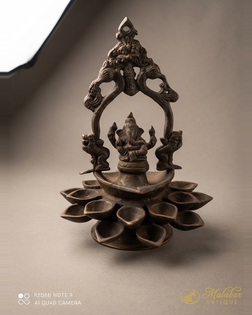 Cast bronze hanging lamp with a deity figure beneath an arch, over a lotus oil bowl.