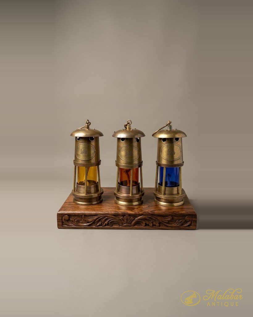 Three brass safety lamps glazed in amber, red and blue on a carved stand.