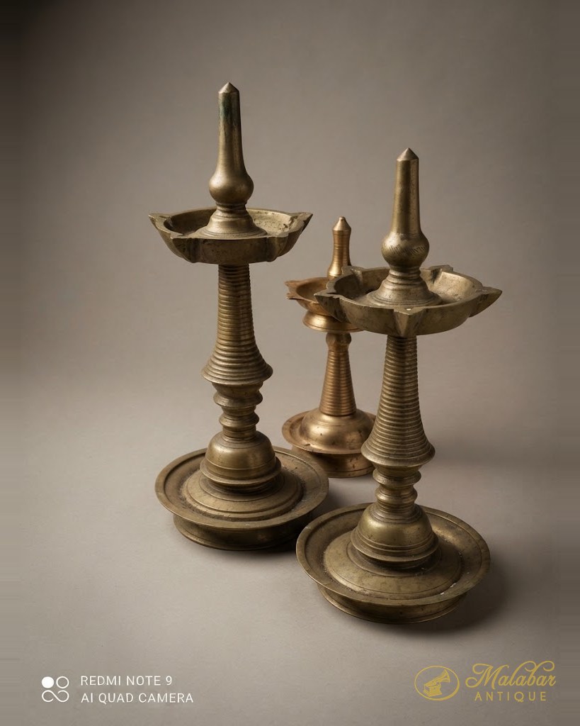 Three traditional Kerala oil lamps on turned brass stems, graduated in height.