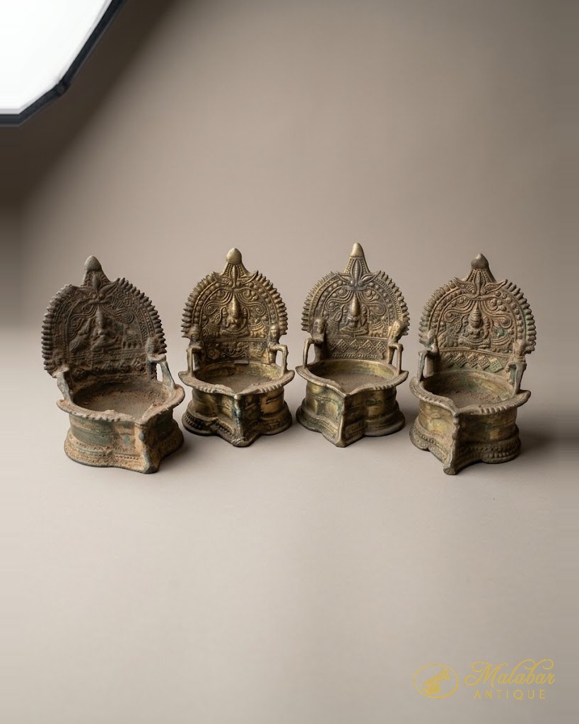 Four cast brass ritual oil lamps with arched backplates, graduated in size.