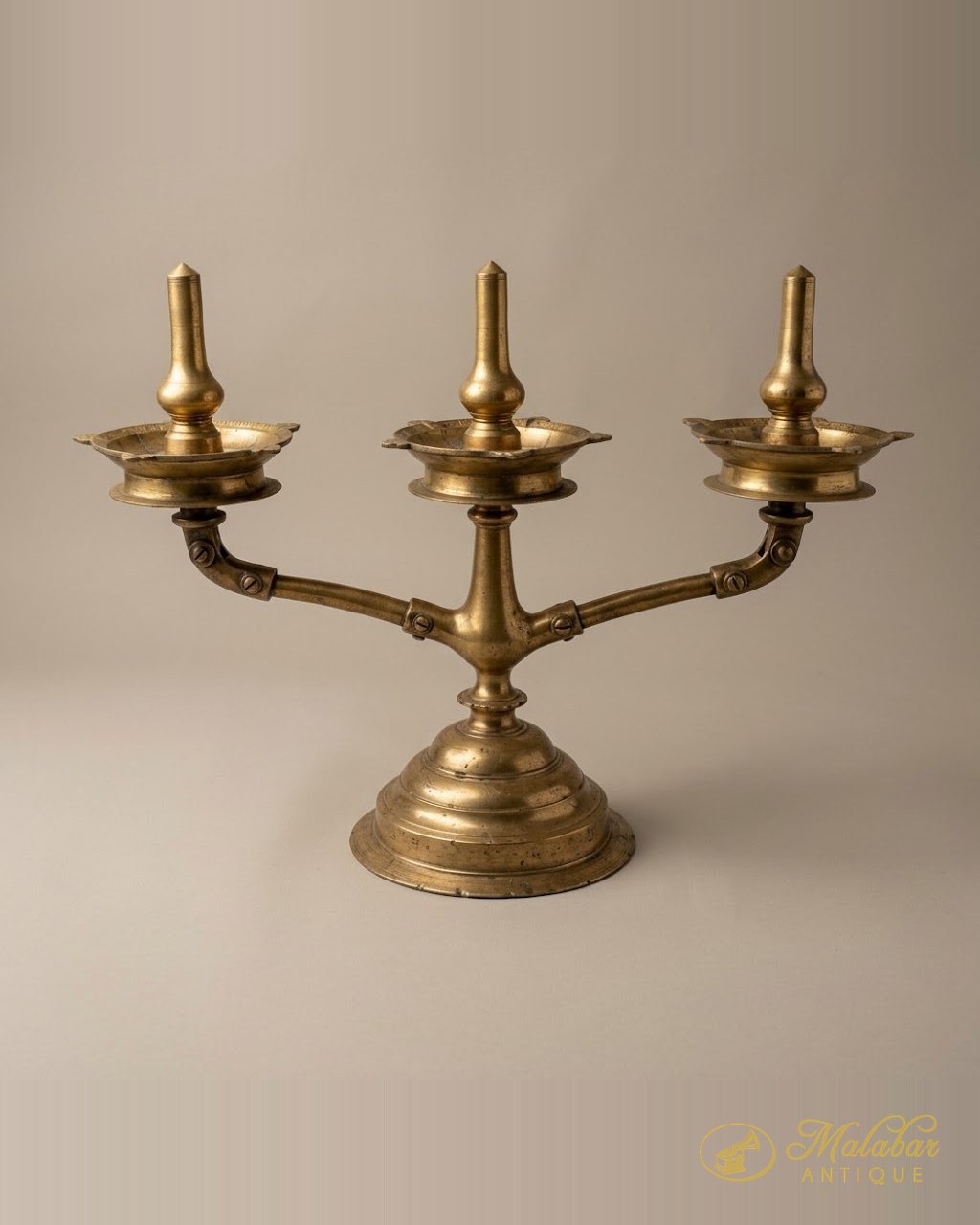 Cast brass oil lamp with three shaped wick bowls on a stepped base.
