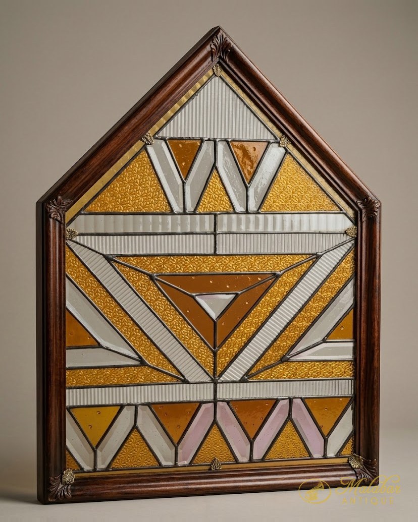Gable-shaped leaded glass panel in amber, white and pink with a geometric chevron and sunray design, in a moulded wooden frame.